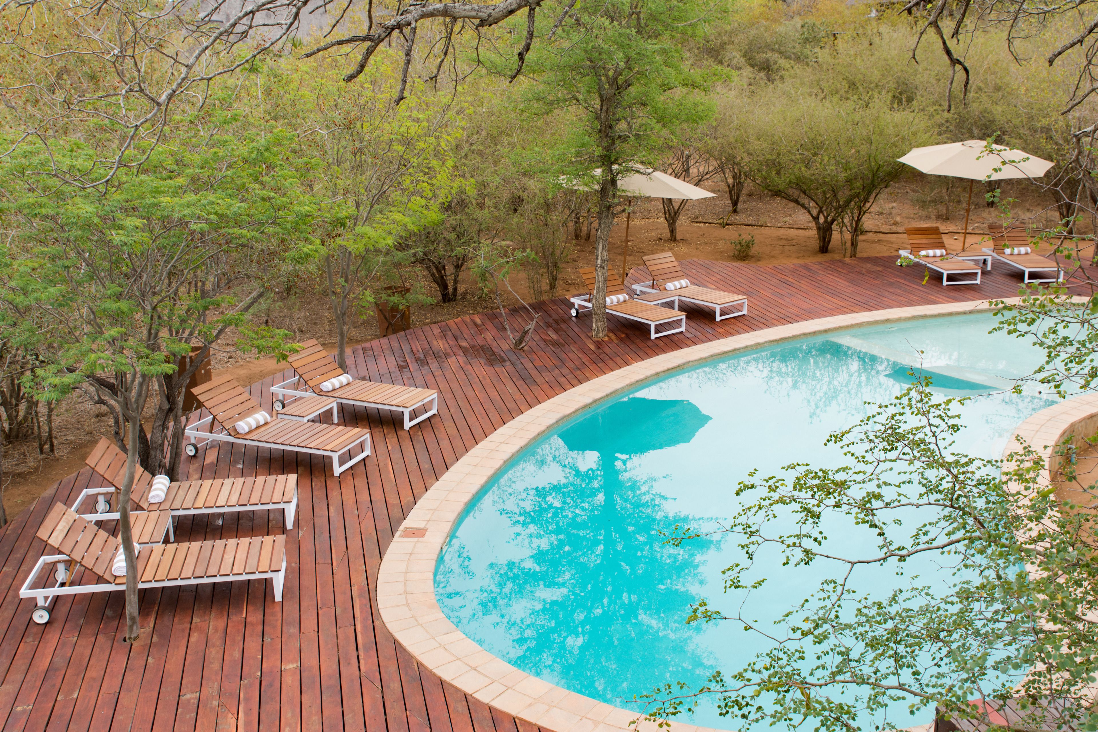 A pool area with wooden deck, lounge chairs, and umbrellas.