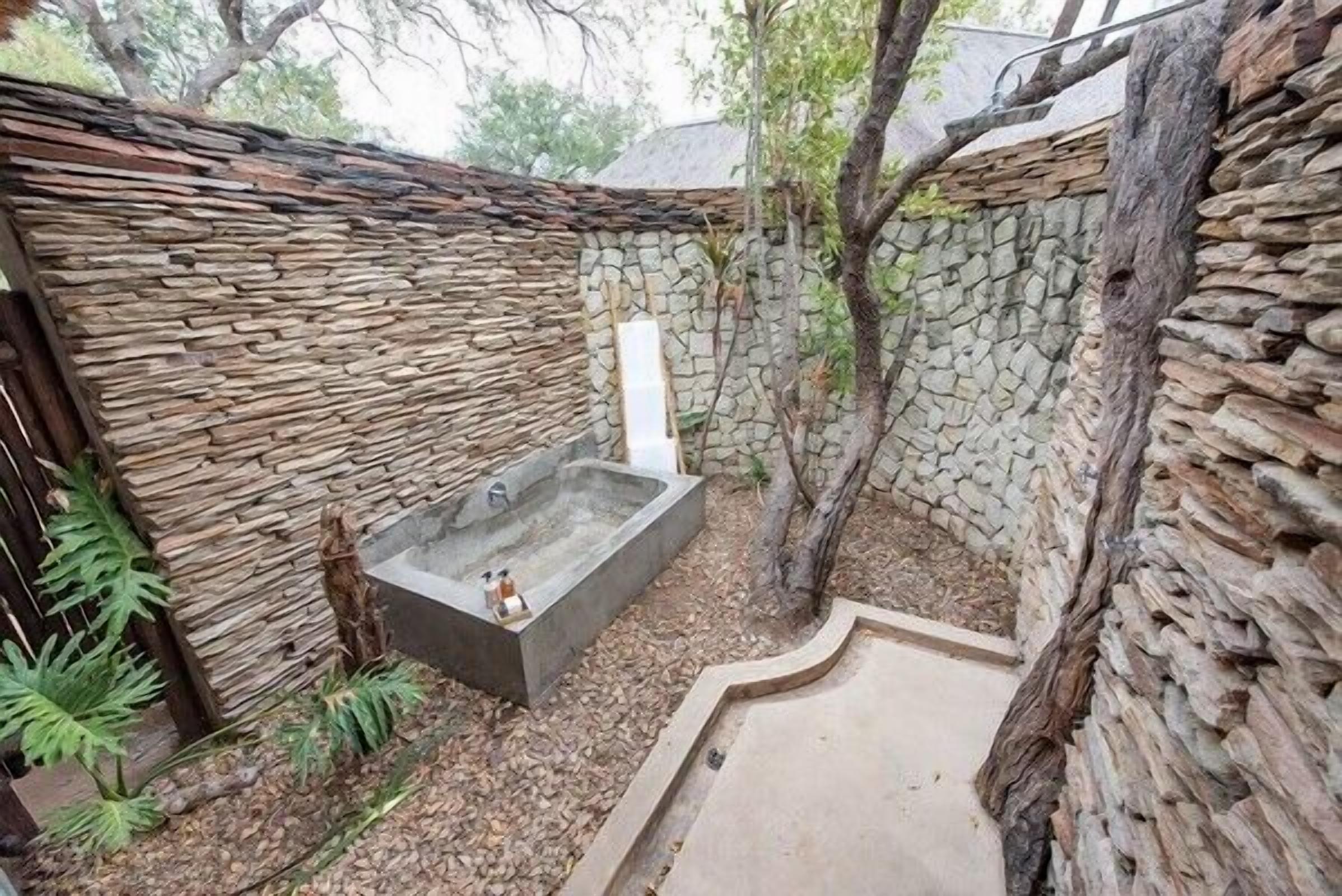 Un espacio al aire libre con paredes de piedra y una bañera de hidromasaje.