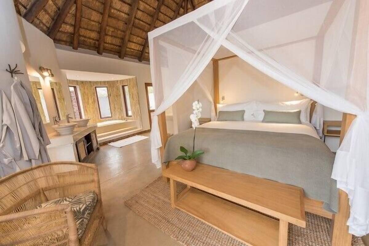 A bedroom with a canopy bed, a bedside table, a chair, and a window.