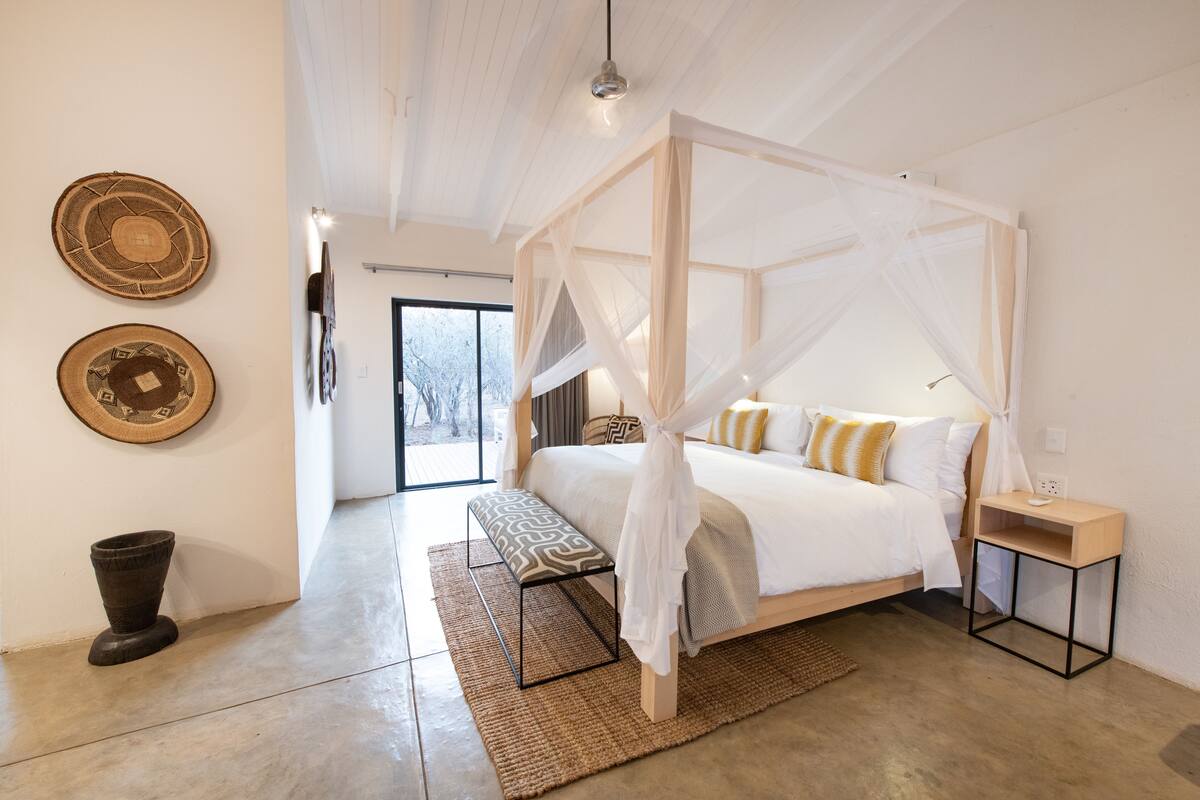 A modern bedroom with a four-poster bed, a bedside table, and a large window.