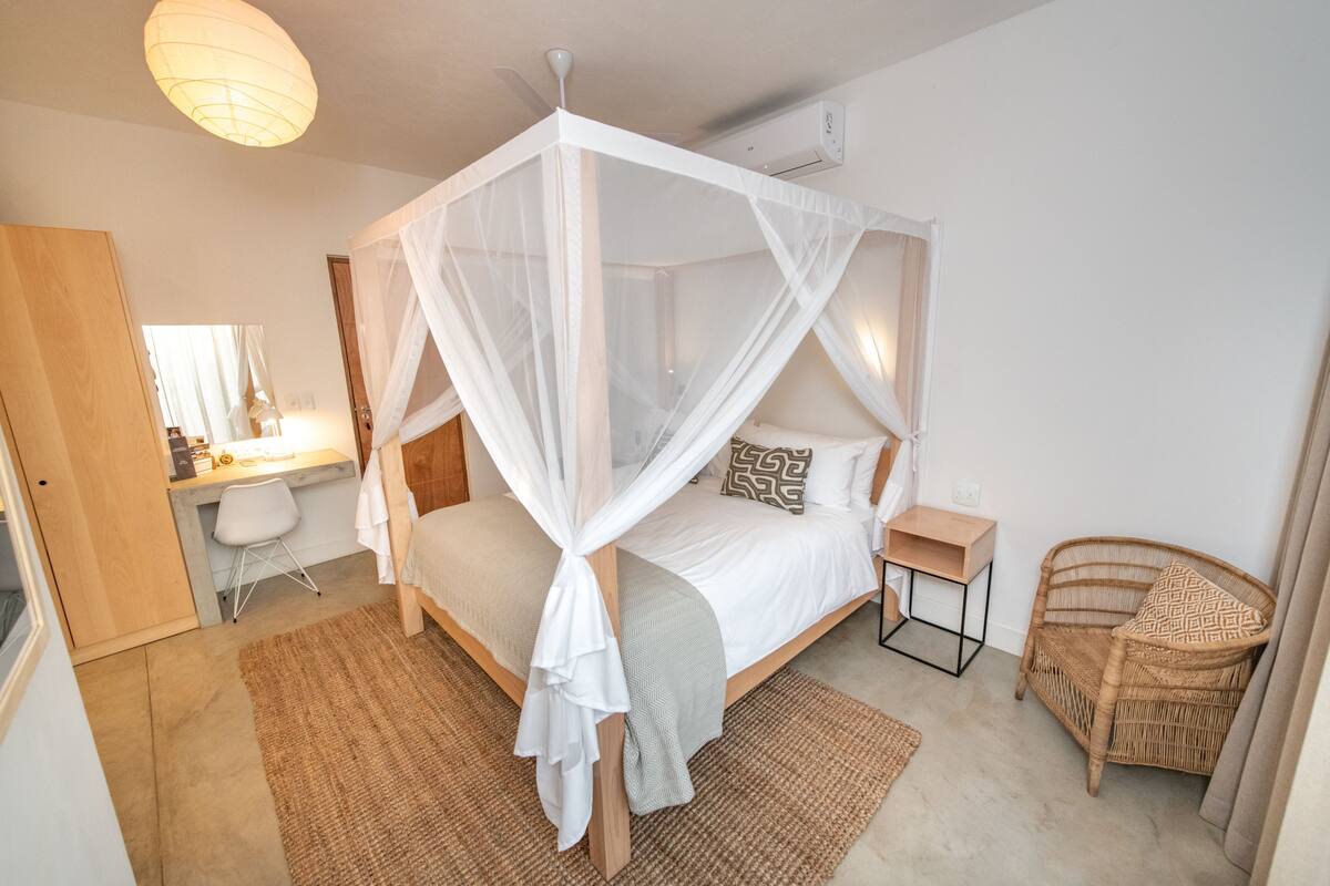 A bedroom with a four-poster bed, a desk, a chair, and a rattan chair.