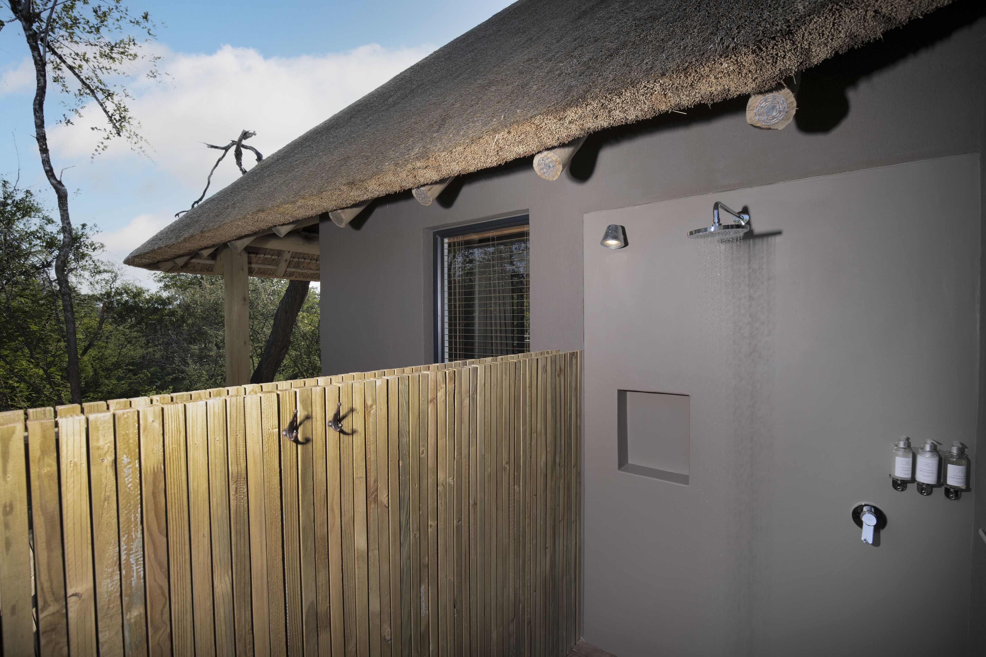 A wooden deck with a thatched roof, a shower area with a wall-mounted faucet, and a window with a metal grid.