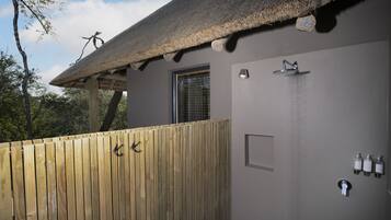 A wooden deck with a thatched roof, a shower area with a wall-mounted faucet, and a window with a metal grid.