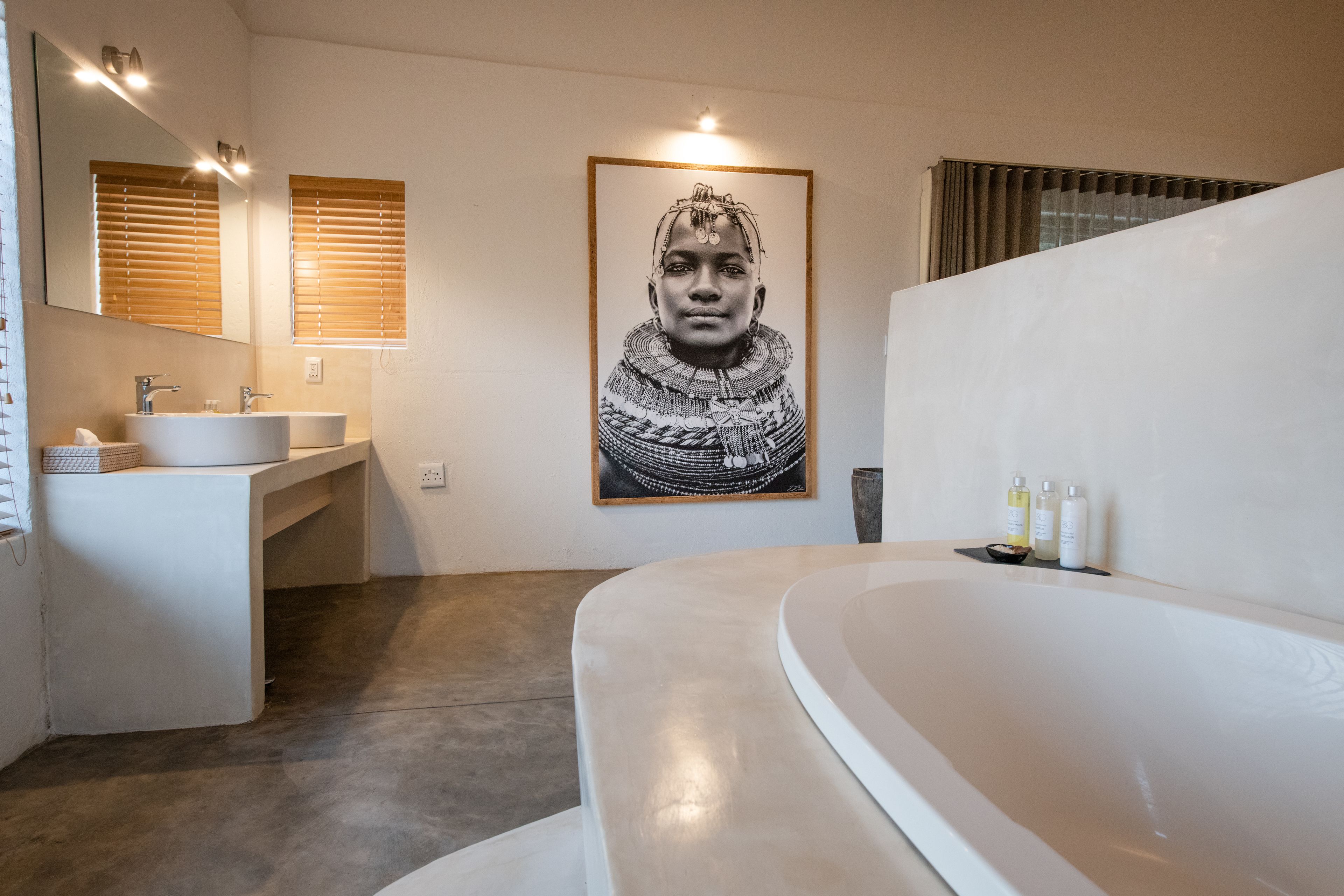 A modern bathroom with a large bathtub, a double sink vanity, and a framed artwork on the wall.