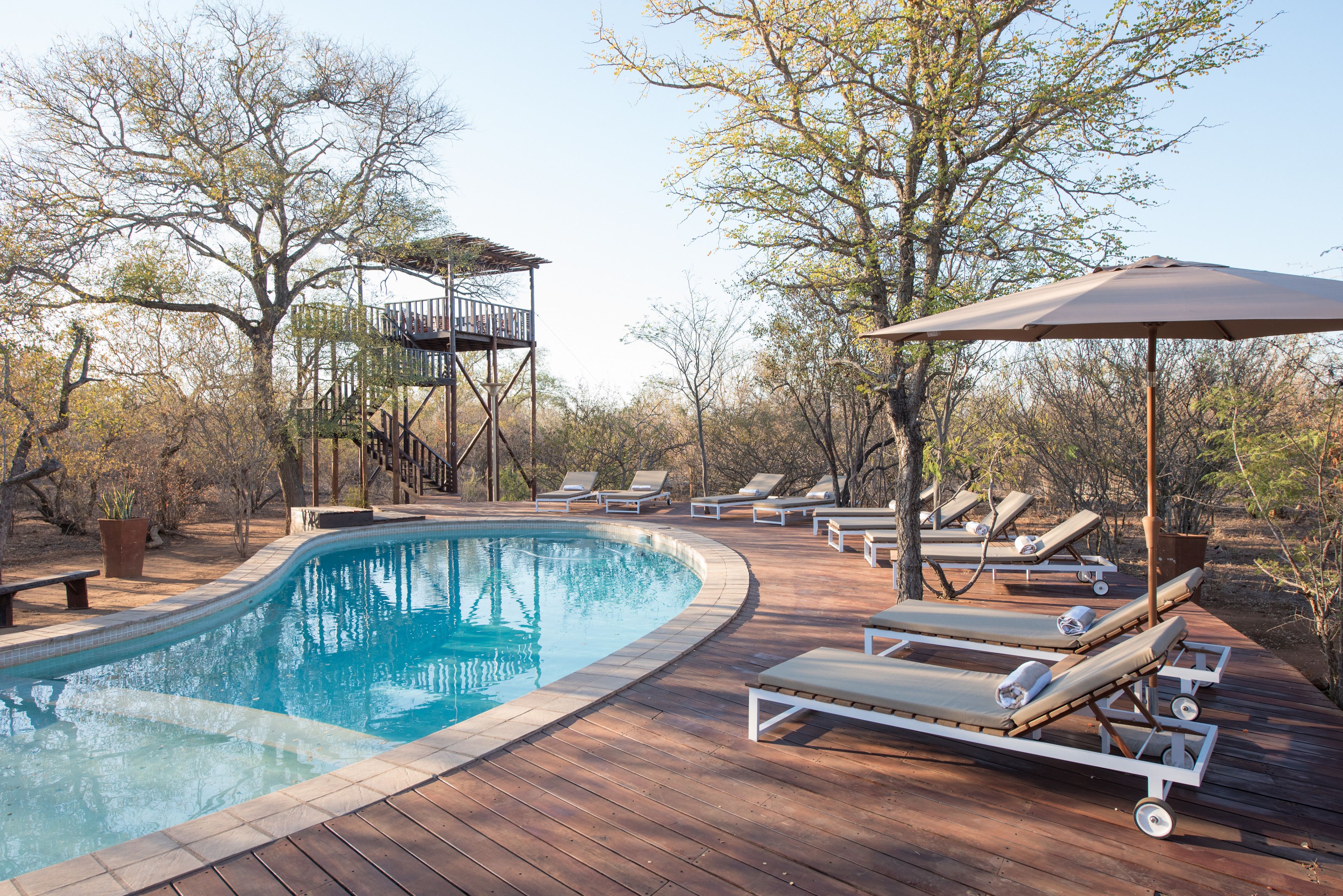 Une terrasse en bois avec une piscine, des chaises longues et un fauteuil de jardin en bois.