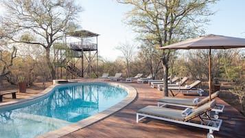 Une terrasse en bois avec une piscine, des chaises longues et un fauteuil de jardin en bois.
