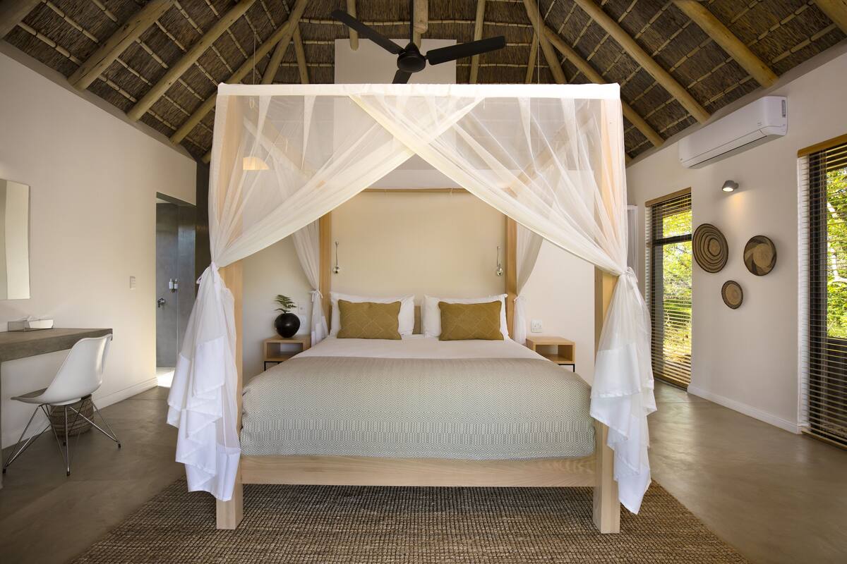 A bedroom with a canopy bed, a desk, and a chair.