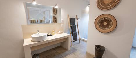 A modern bathroom with a large mirror, a sink, and two decorative woven baskets on the wall.