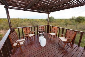 Una terraza de madera con cuatro sillas y una mesa, con vistas a un paisaje natural.