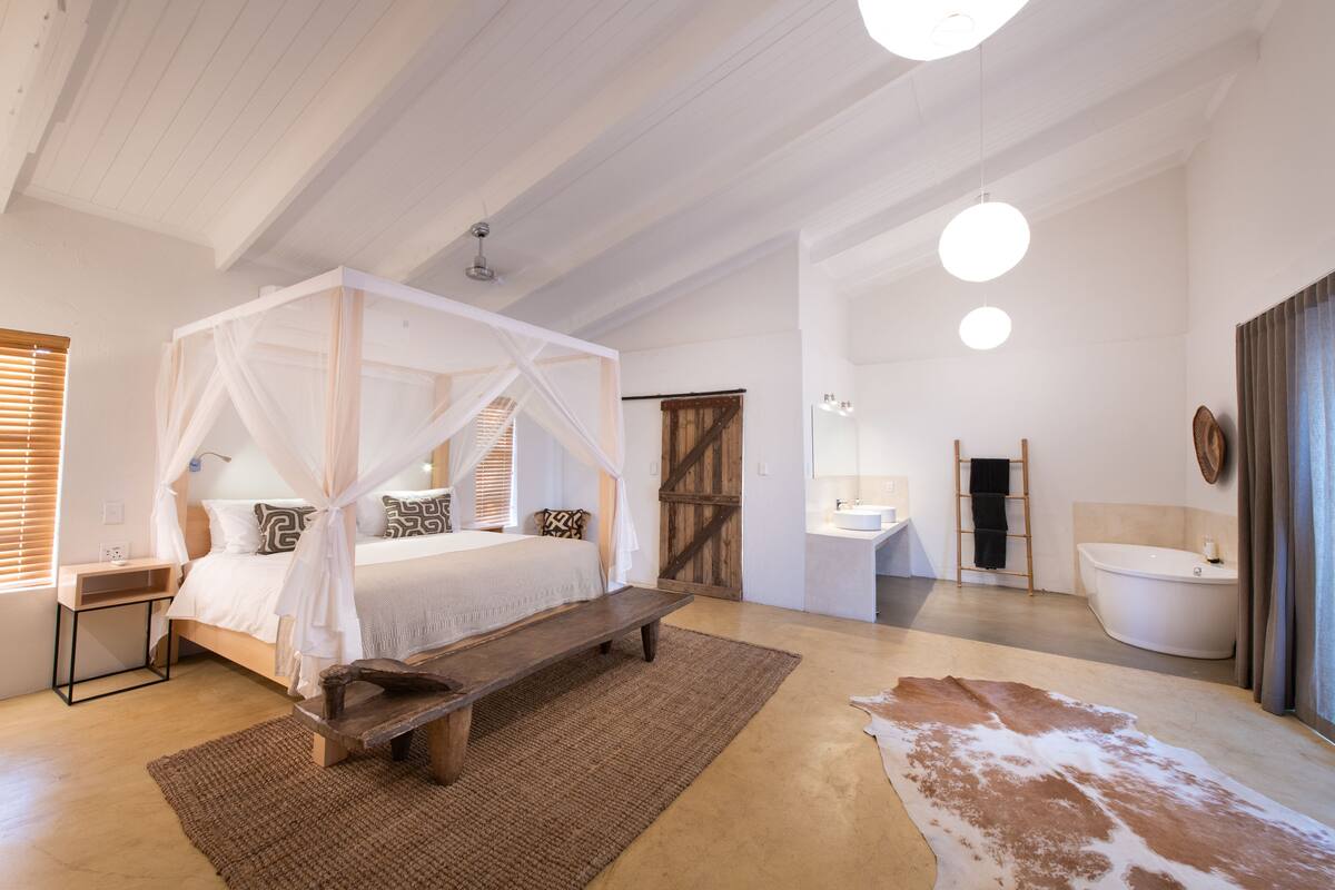 A spacious bedroom with a four-poster bed, a wooden bench, and a large rug.