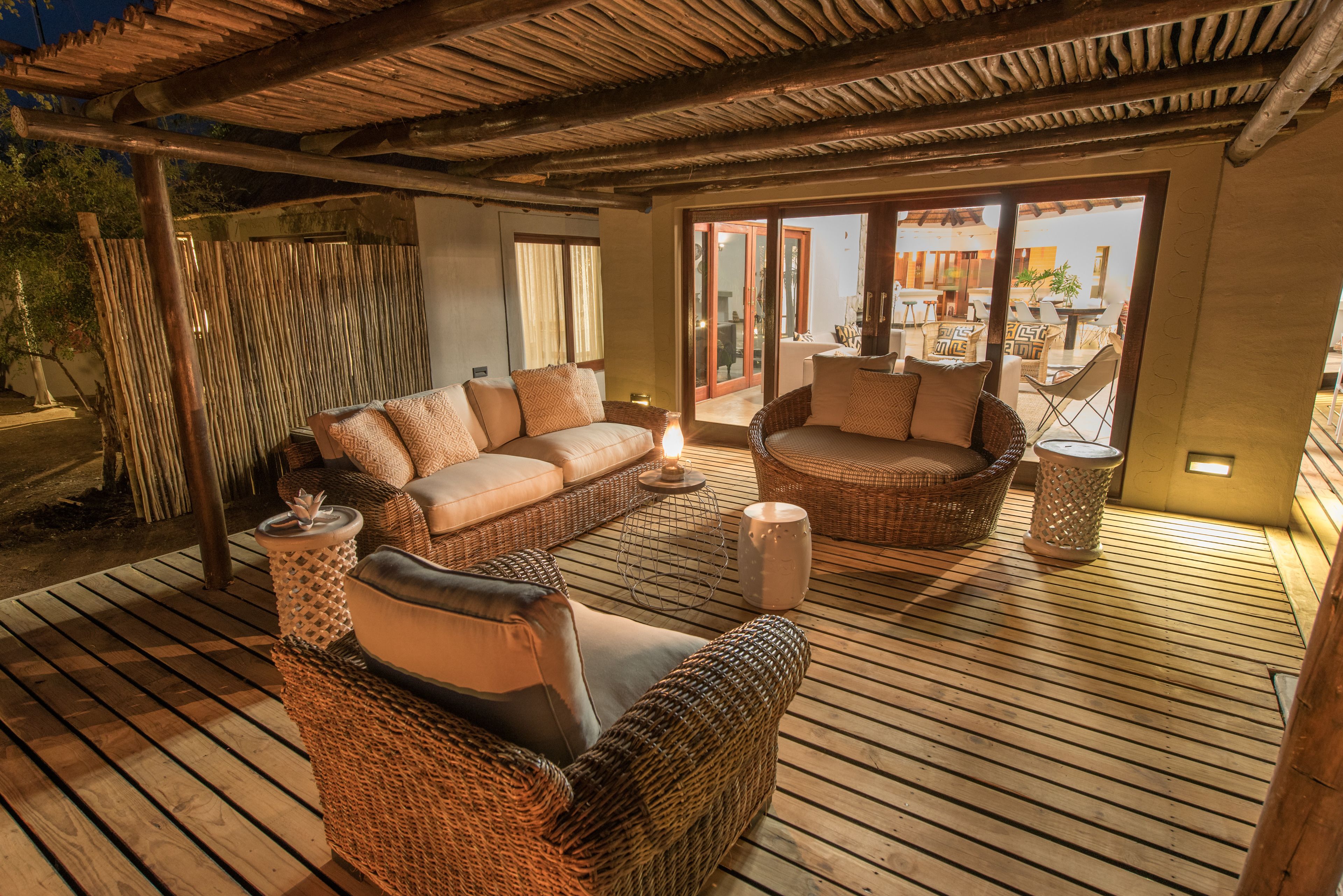 Una terraza de madera con muebles de mimbre, incluyendo sofás y una silla, y un vidrio que da al exterior.