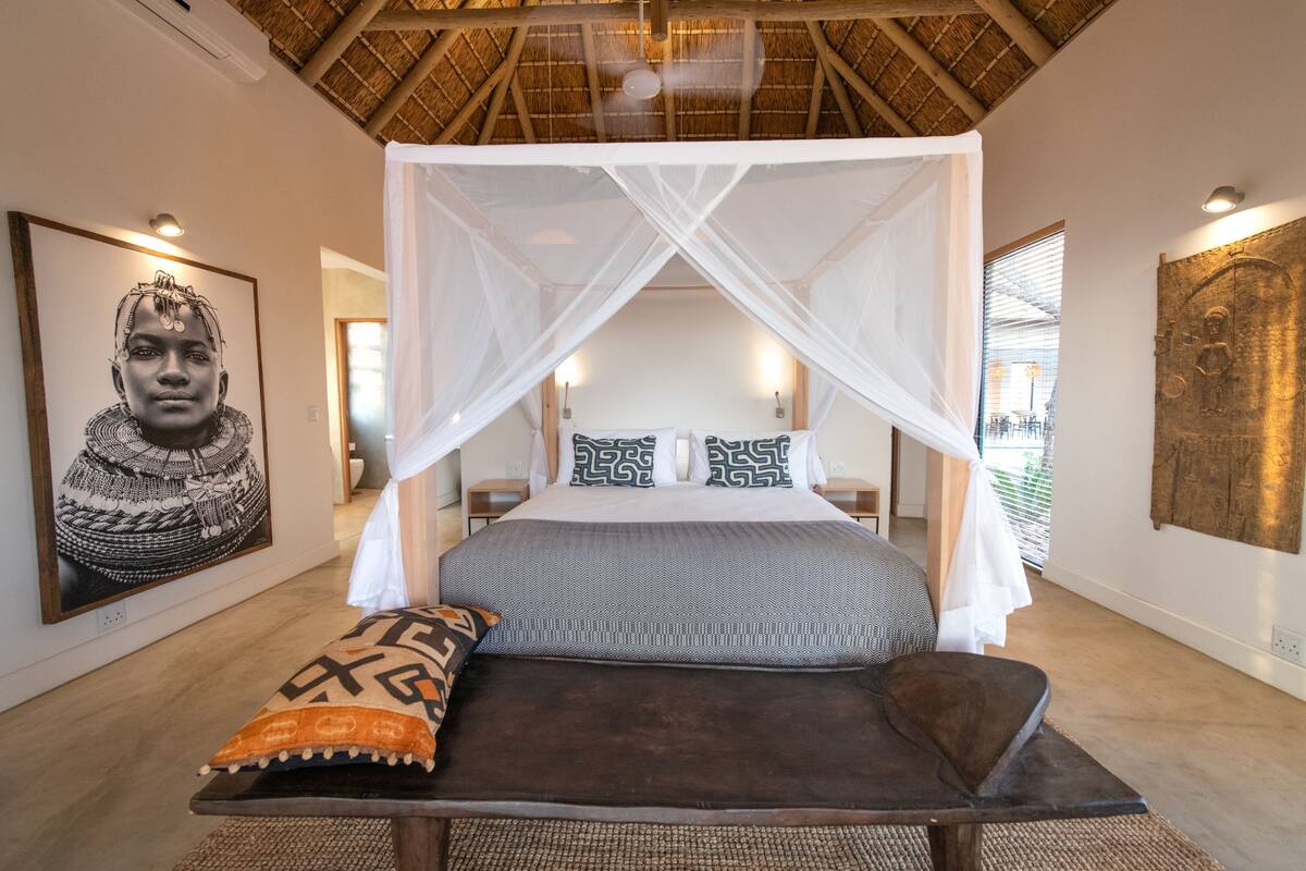 A bed with a canopy, a pillow, a bench, and artwork on the walls.