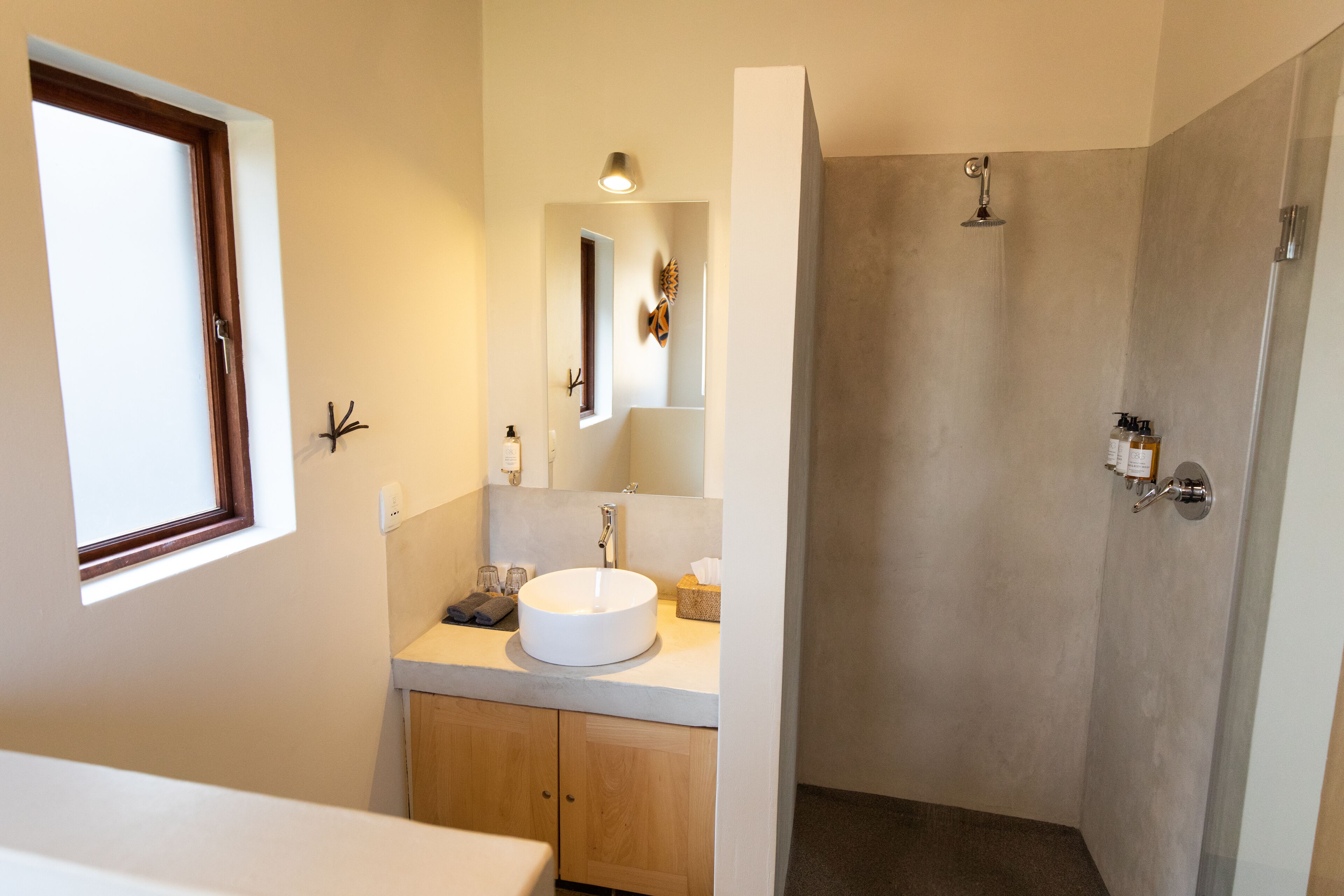 A modern bathroom with a large window, a round sink, a mirror, and a shower area.