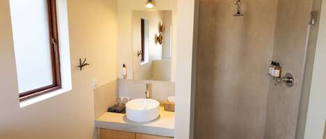 A modern bathroom with a large window, a round sink, a mirror, and a shower area.