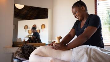 Experience a soothing massage in a serene space with a massage table, wooden ceiling, and a large mirror.