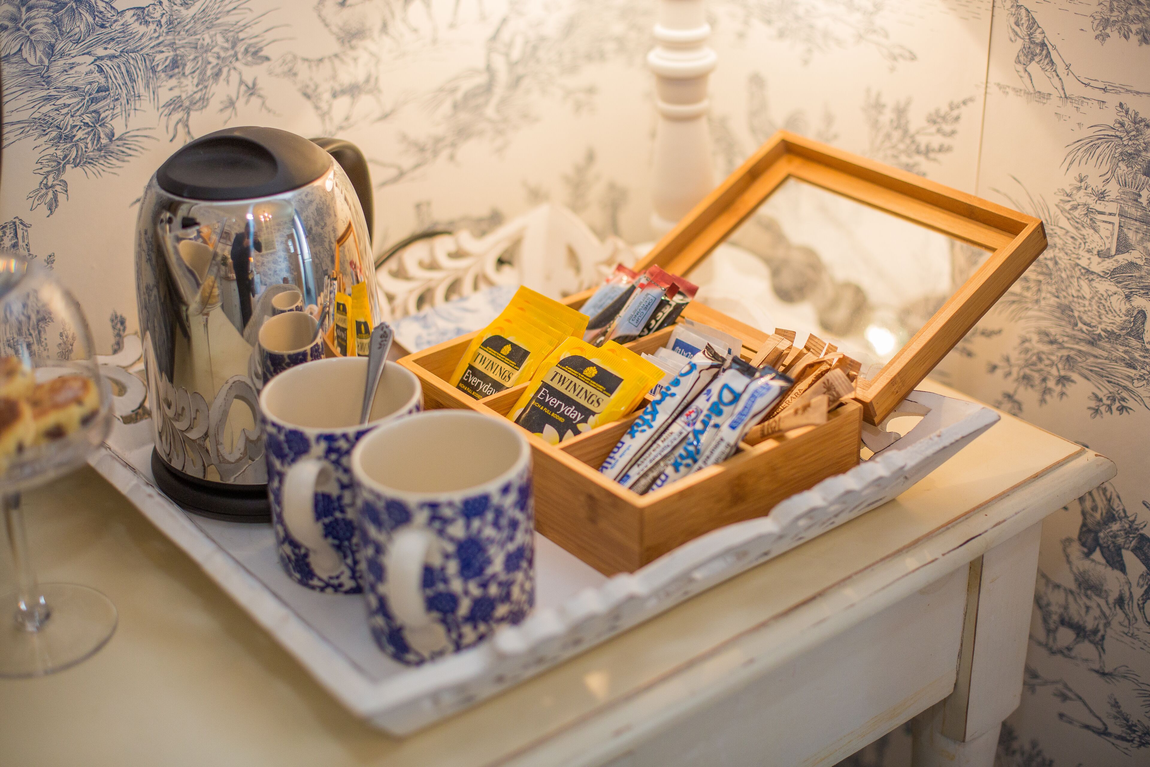 Un tavolo con una caffettiera, due tazze bianche e azzurre decorate, un vassoio con una scatola di legno contenente diversi oggetti e una cornice con un'immagine.