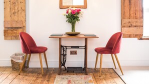Et værelse med et træbord, to røde stole, en vase med blomster, en symaskine og en hængende lampe.