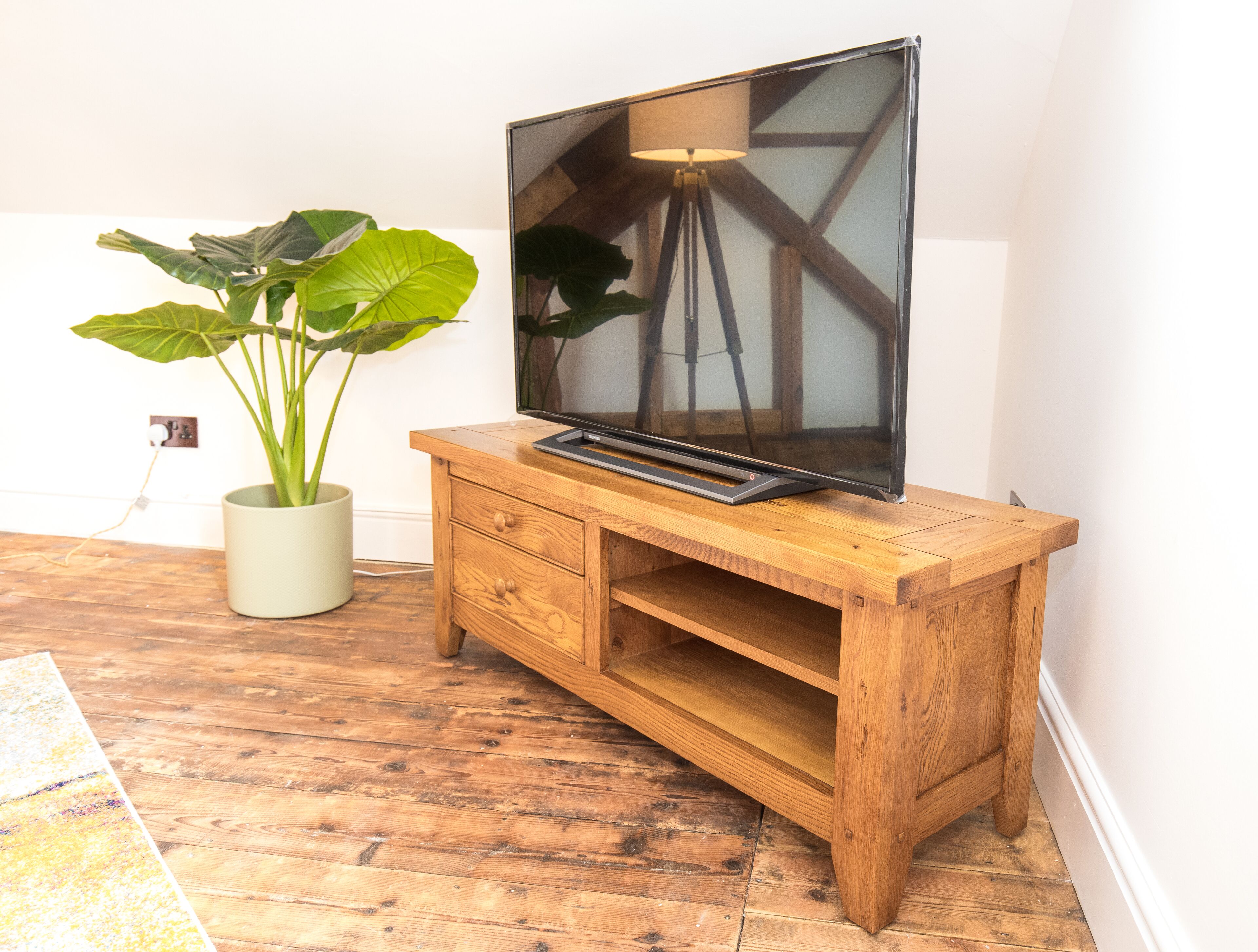 A wooden TV stand with a flat-screen TV, a potted plant, and a wooden floor.