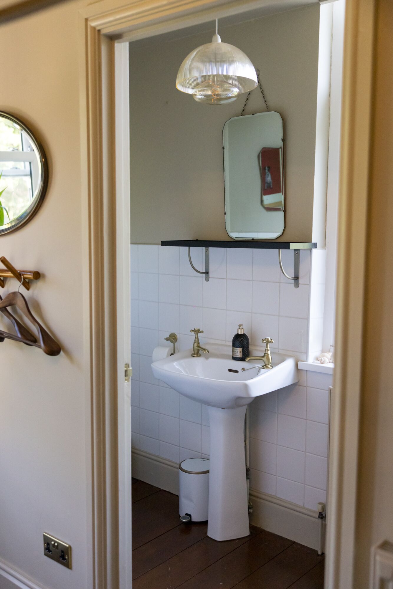 Casa de banho com lavatório branco, duas torneiras douradas, um espelho sobre o lavatório e um candeeiro suspenso.