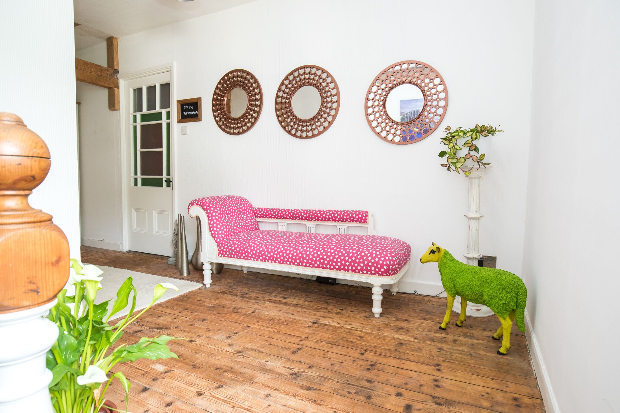 Una habitación con piso de madera, un sofá blanco con funda de lunares rojos y tres espejos redondos en la pared.