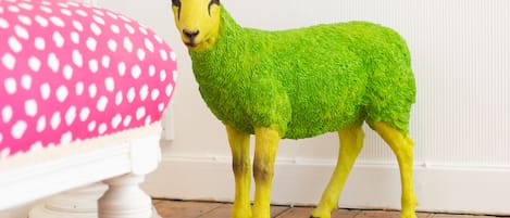 En grön fårfigur som står bredvid ett vitt bord med en rosa duk med prickar.