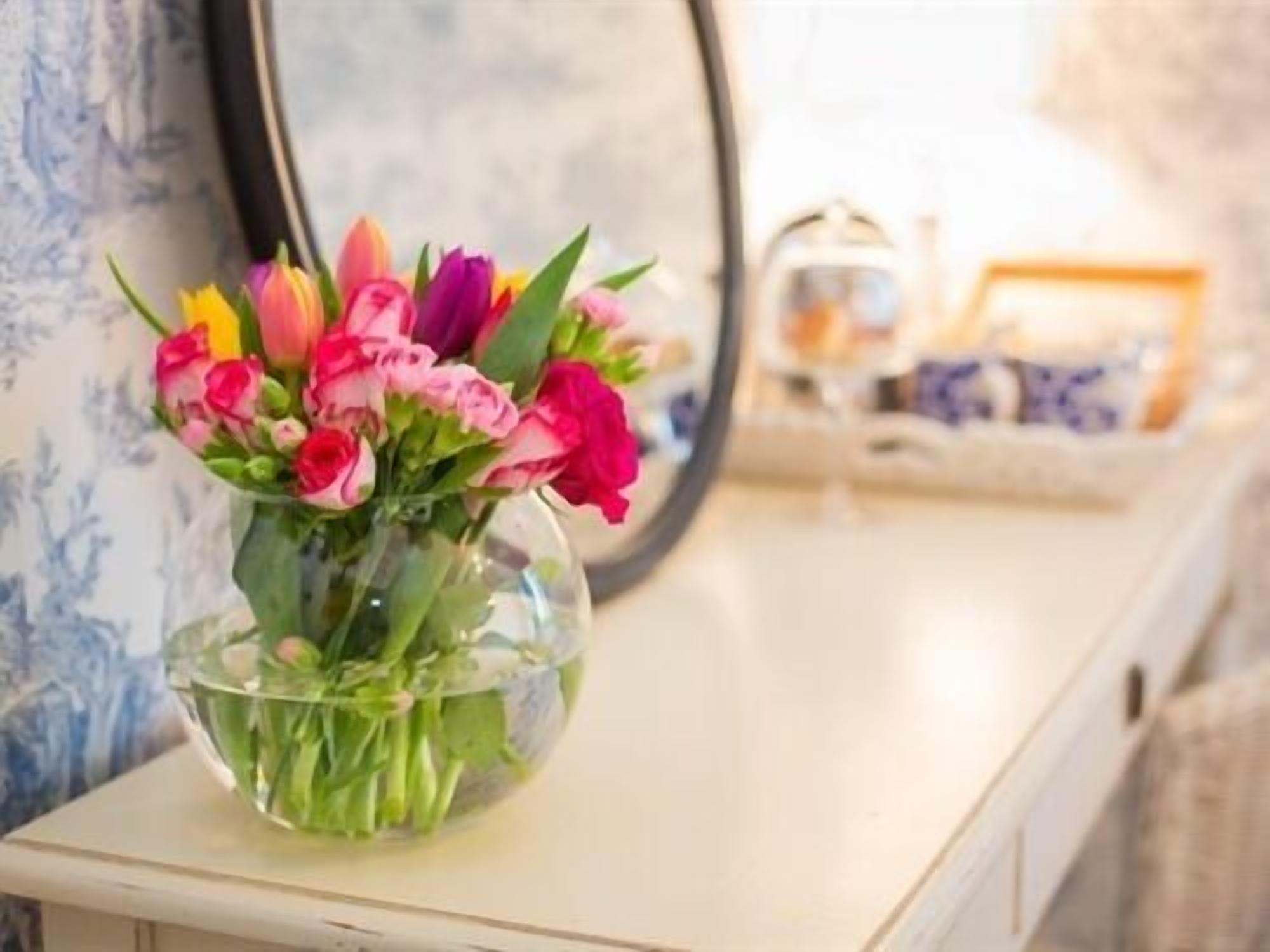 A clear glass vase with pink and purple flowers on a white surface.