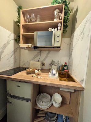 A compact kitchen with a built-in microwave, a sink, and a countertop with a dish rack.