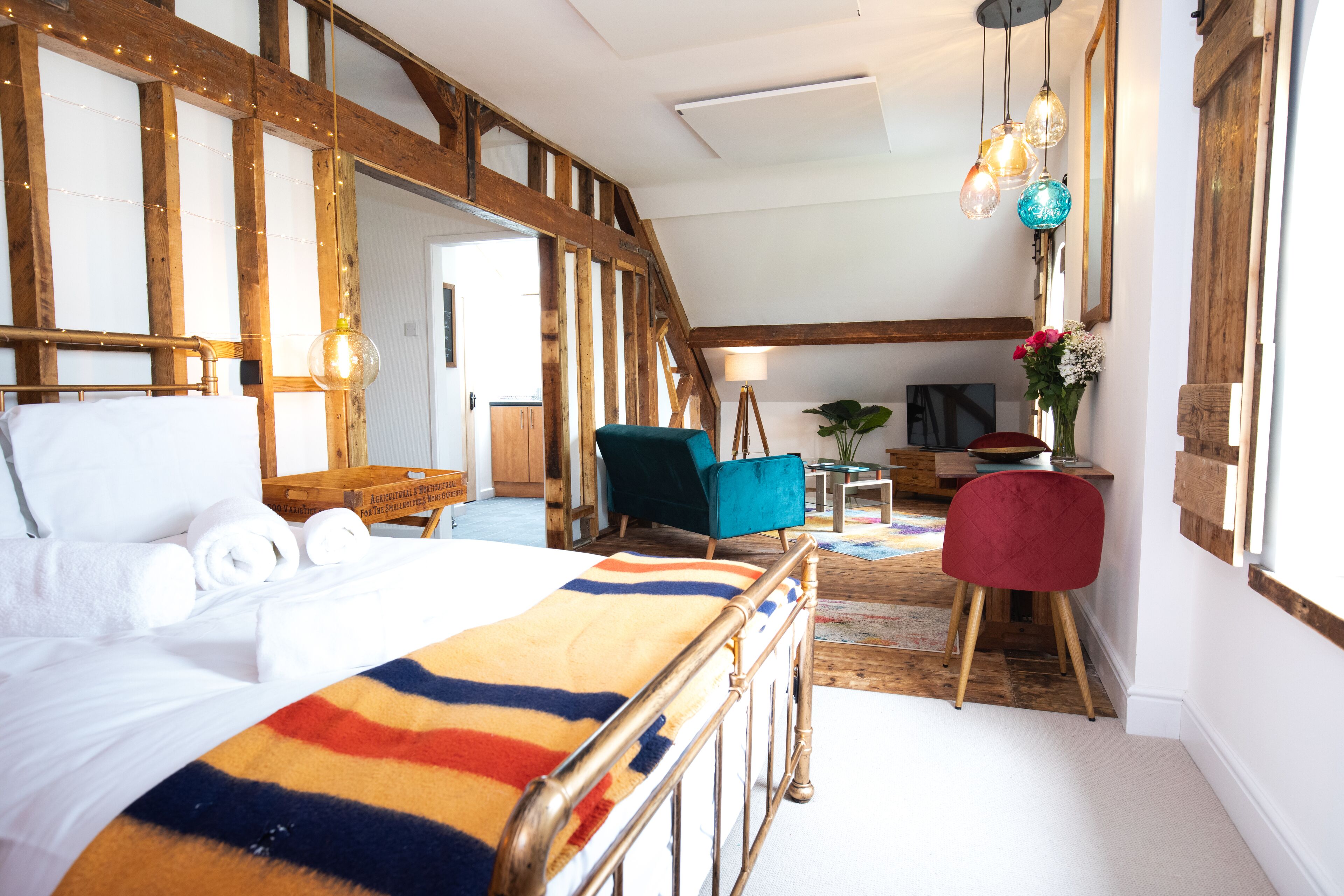 A bedroom with a bed, a colorful blanket, a wooden ceiling, and a desk with a chair.