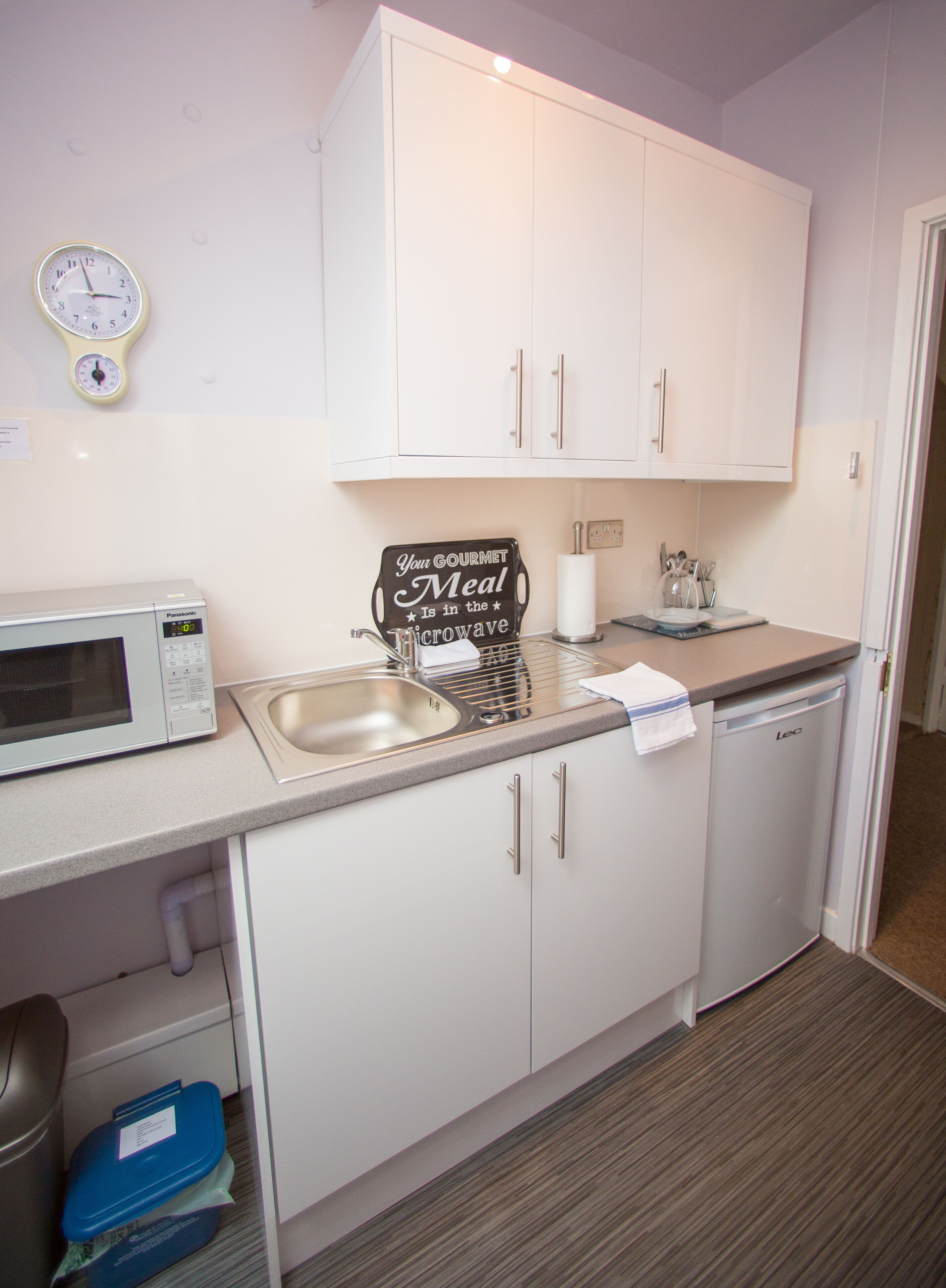A compact kitchen with white cabinets, a microwave, a sink, and a dishwashing machine.