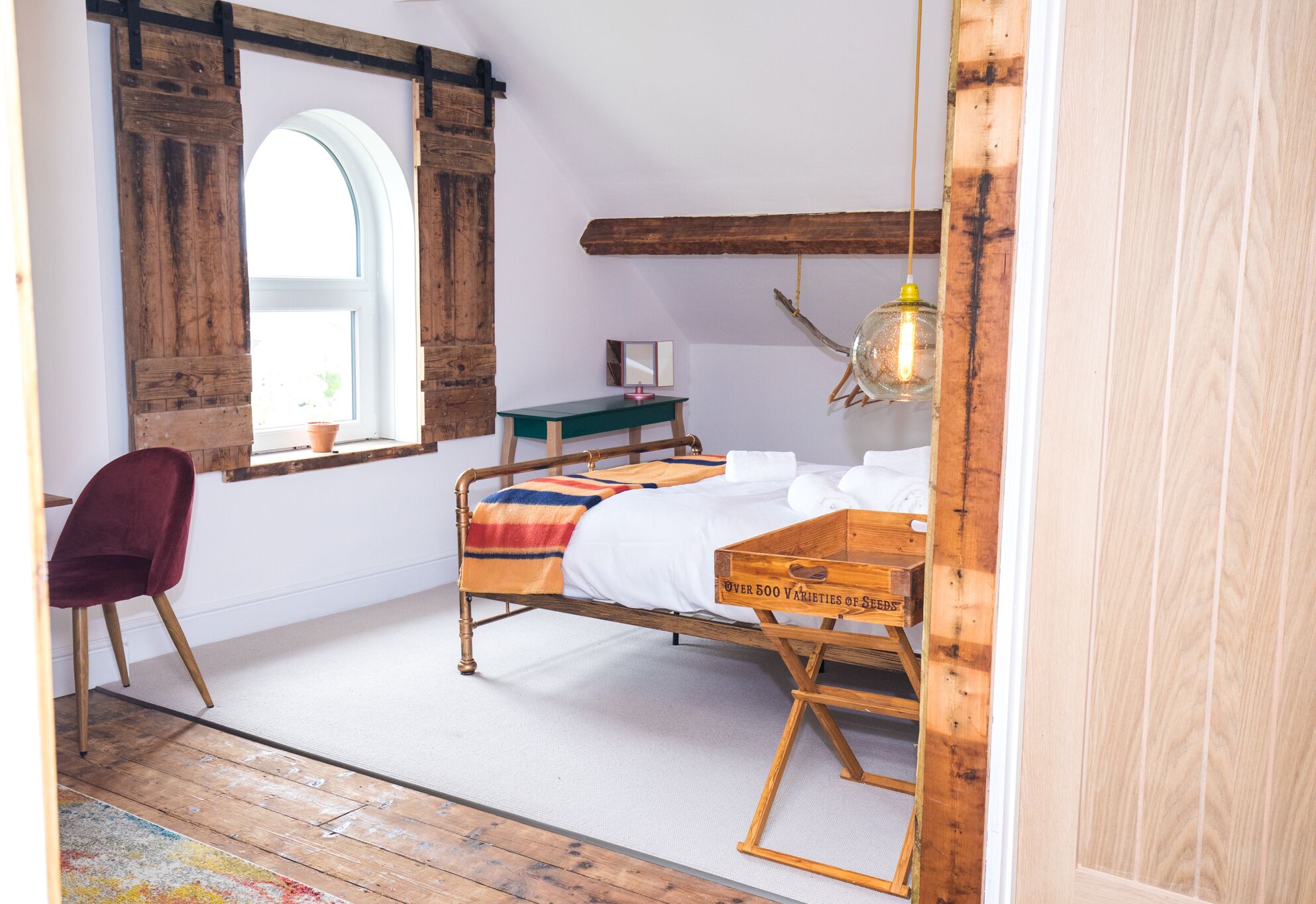 Ein Schlafzimmer mit einem hölzernen Bett, einem Schreibtisch, einem Stuhl, einem Fenster und einer Pendelleuchte.