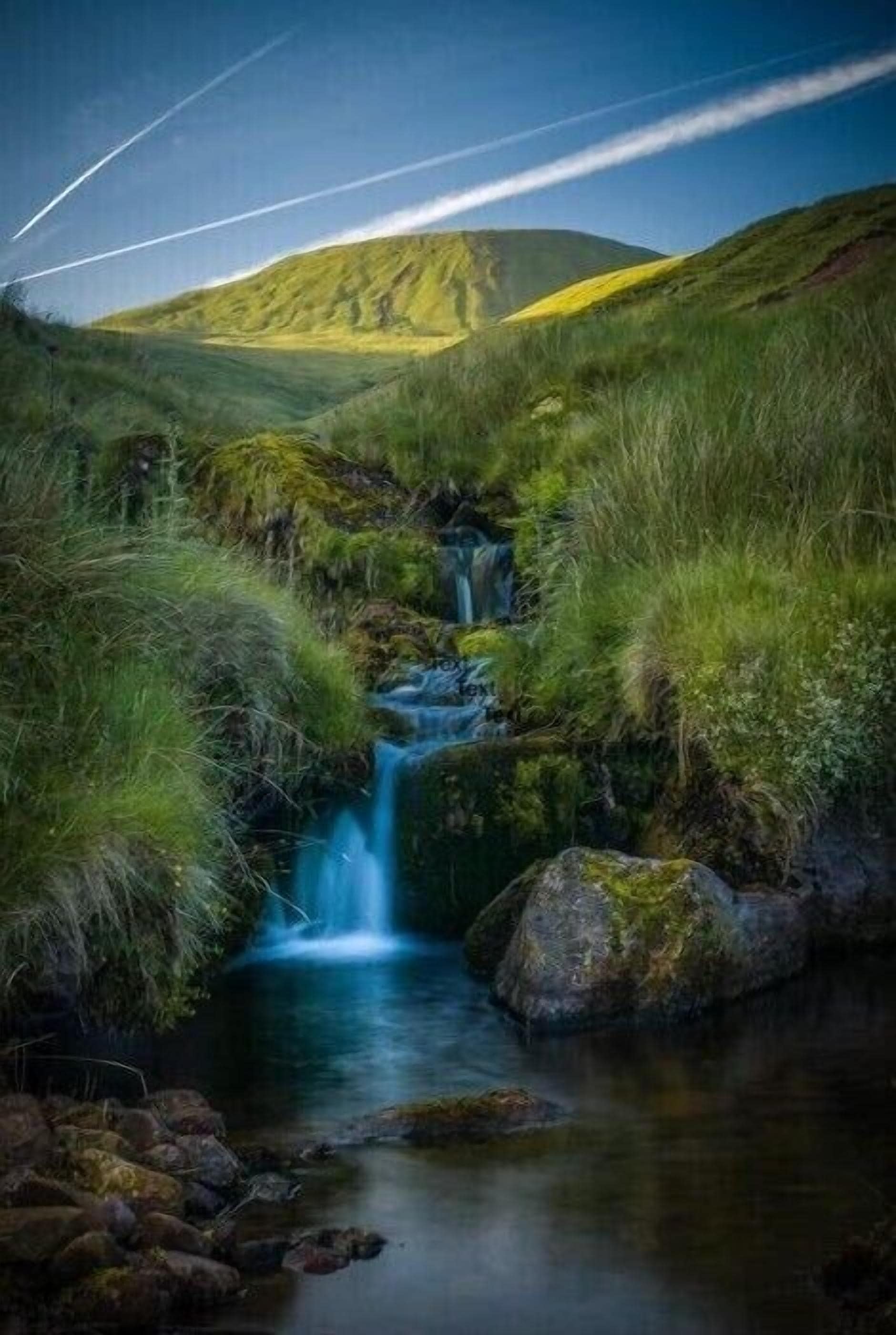 Un paisaje sereno con una cascada pequeña, rodeado de hierba verde exuberante y rocas.