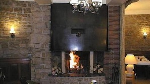 A stone-walled room with a fireplace, a chandelier, and a round table with chairs. - Hôtel de Paris (Poligny)