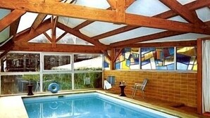 An indoor swimming pool with wooden beams, a tiled wall, and a window with a view. - Hôtel de Paris (Poligny)