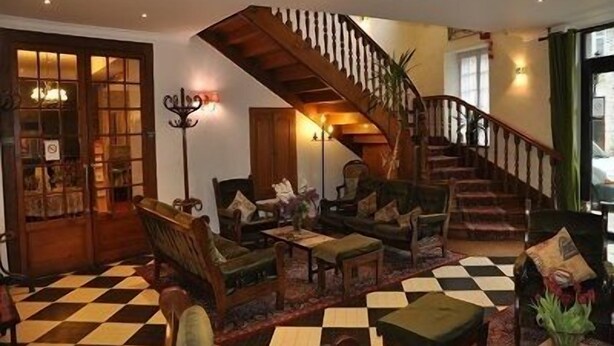 A cozy lobby with a checkered floor, a staircase, and a seating area with a fireplace. - Hôtel de Paris (Poligny)
