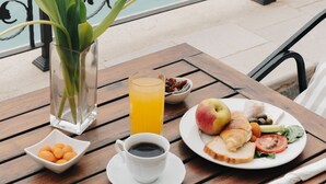 Una mesa con alimentos para el desayuno, un vaso de zumo de naranja, una taza de café, y un plato con un croissant, una manzana y verduras.