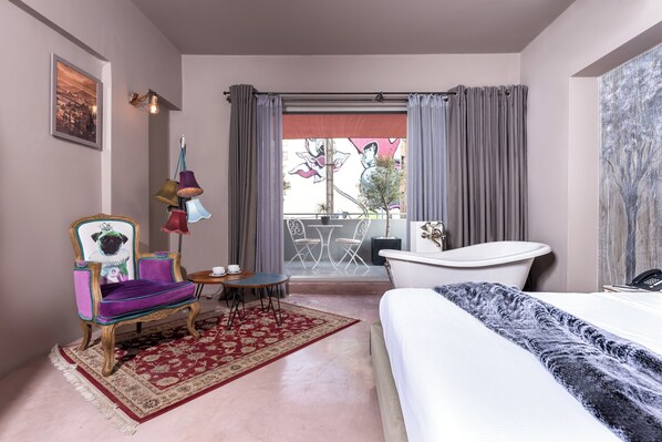 Habitación de hotel con cama, una silla, una mesa, lámpara, bañera y vistas al exterior.