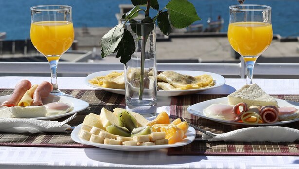 Una mesa con alimentos para el desayuno y una rosa, con vista a un cuerpo de agua.