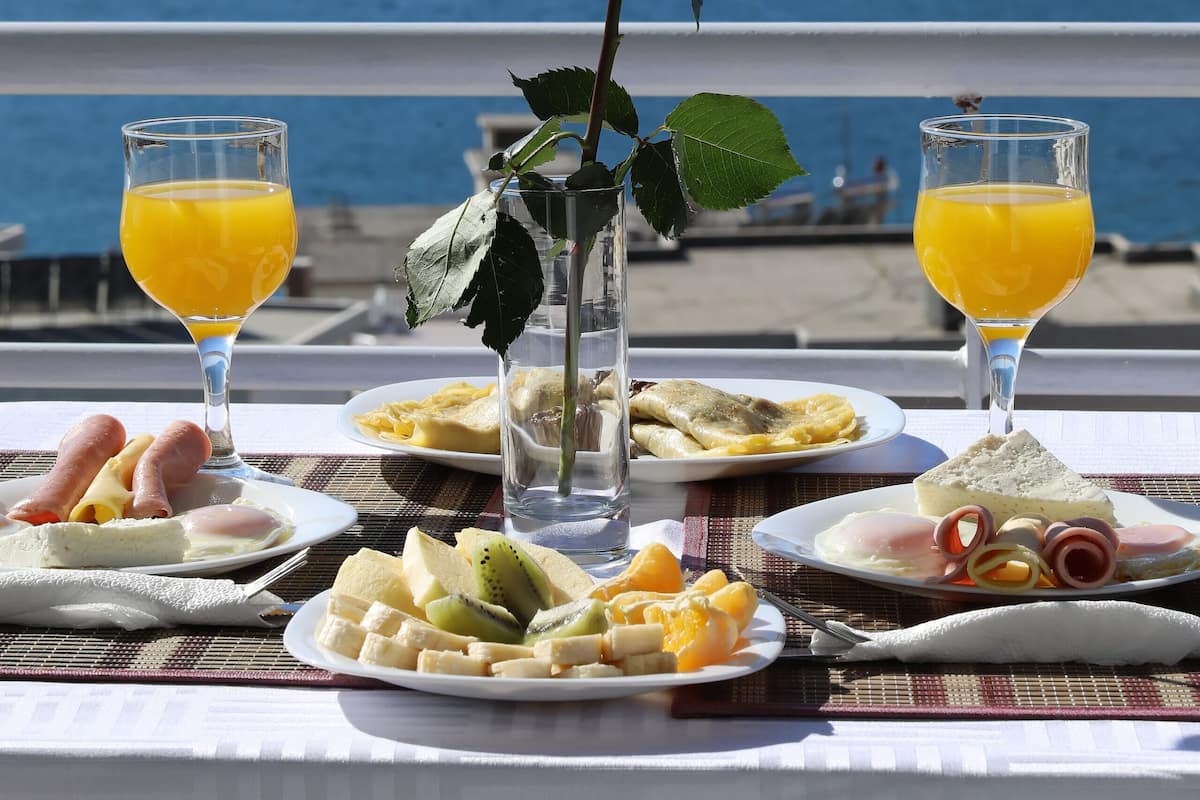 A table with breakfast items and a rose, overlooking a body of water.