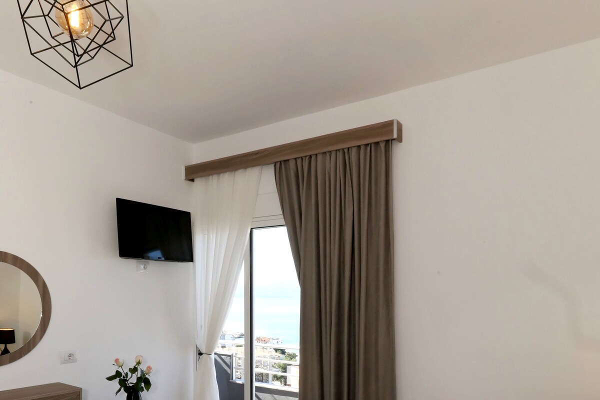Habitación de hotel con cama, escritorio, televisor, espejo y vista a la ciudad.