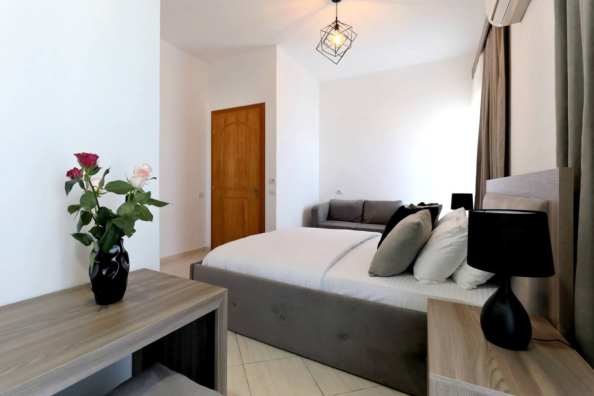 A bedroom with a bed, bedside table, lamp, and a potted plant.