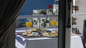 Una mesa en el balcón con mantel blanco, dos vasos de jugo de naranja, un plato de comida y una rosa roja.