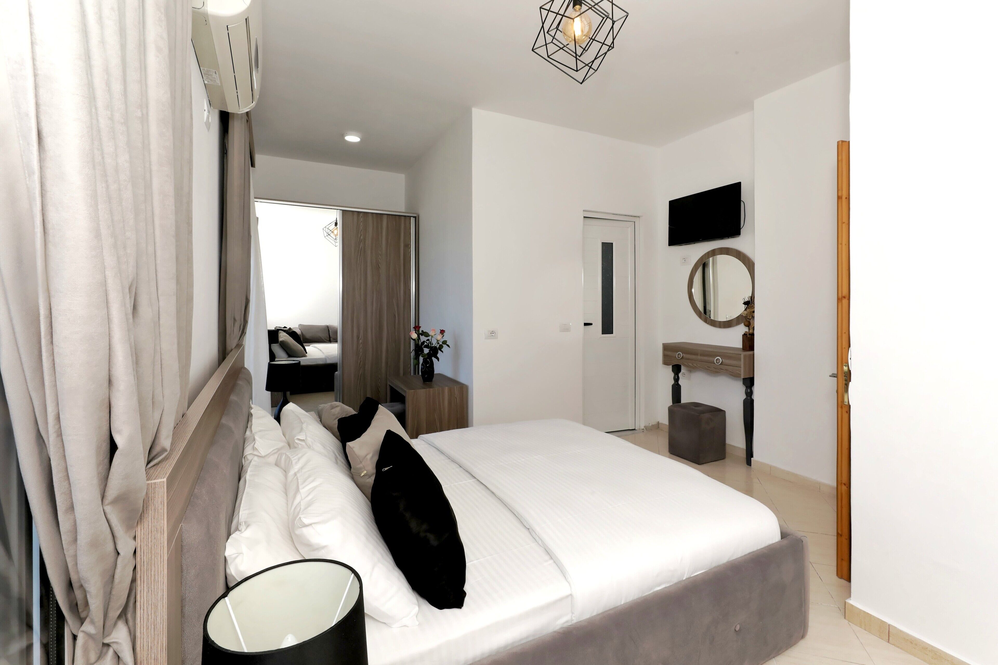 Une chambre à coucher comprenant un lit, une table de chevet, une lampe, un appareil de climatisation et un téléviseur fixé au mur.