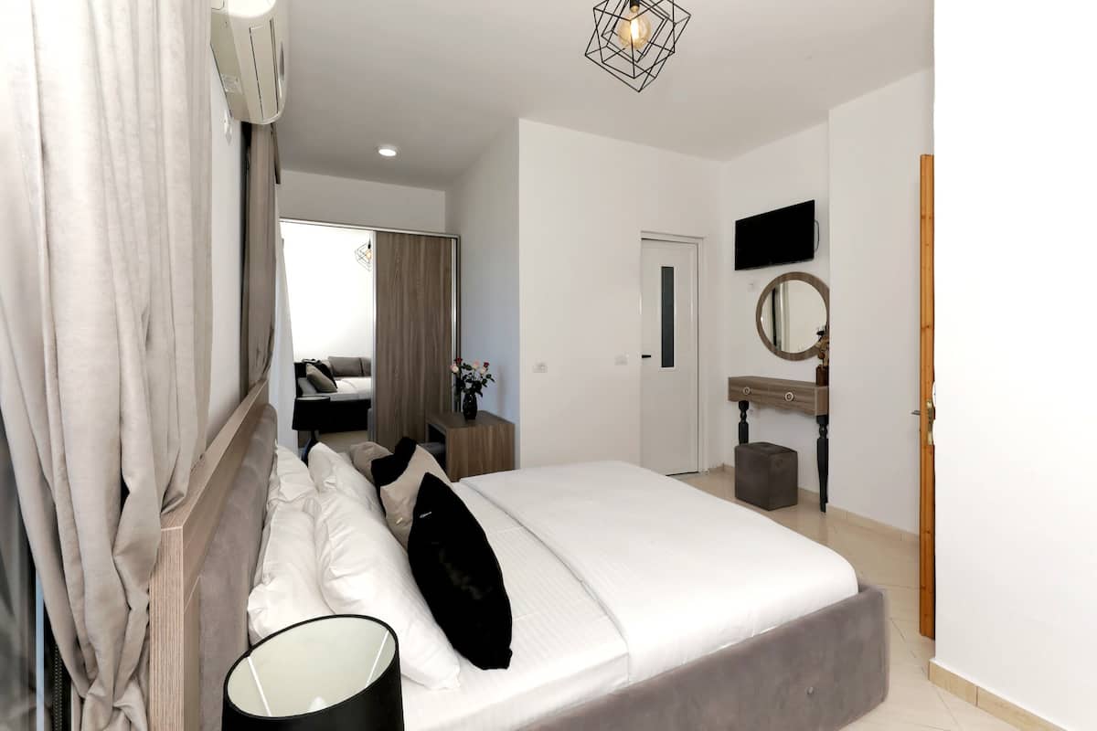 A bedroom with a bed, bedside table, lamp, air conditioning unit, and a television on the wall.