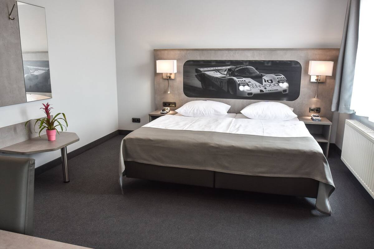 Een hotelkamer met een groot bed, twee nachtkastjes met lampen, een kamerplant en een grote spiegel.