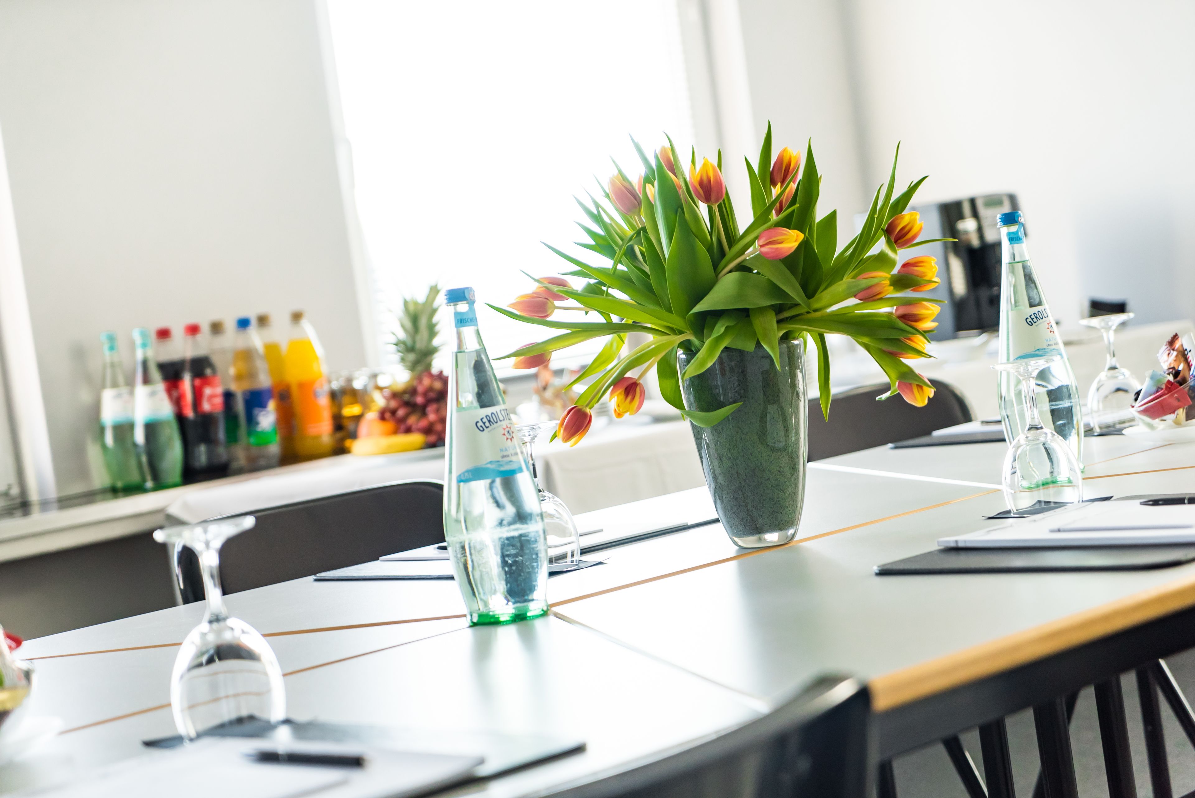 A conference table with a vase of tulips, water bottles, and a glass carafe.