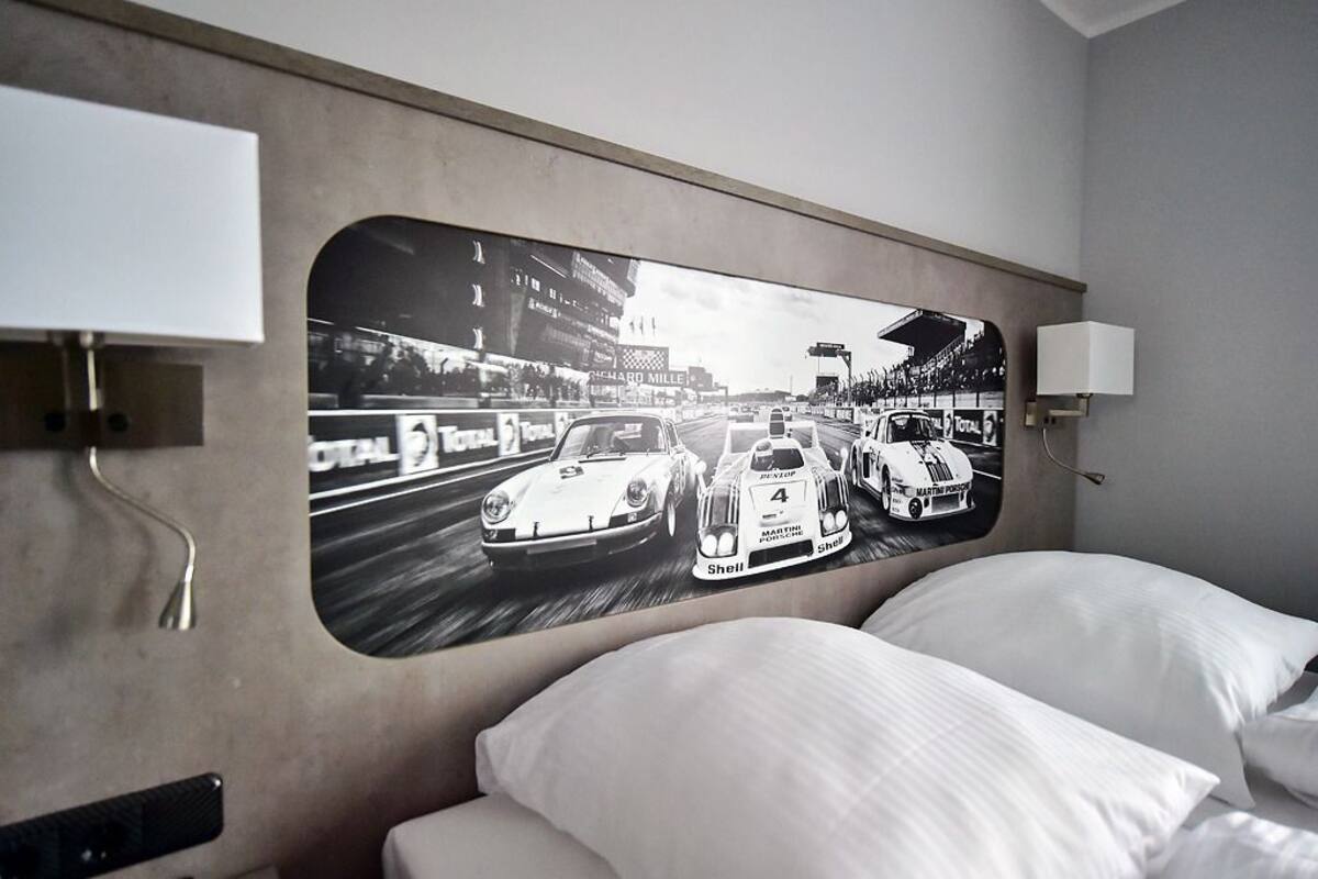 Een hotelkamer met een groot muurschildering van raceauto's, een bed met witte lakens en een moderne lamp.