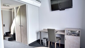 A modern room with a round table, a desk, a chair, a TV, and a staircase.
