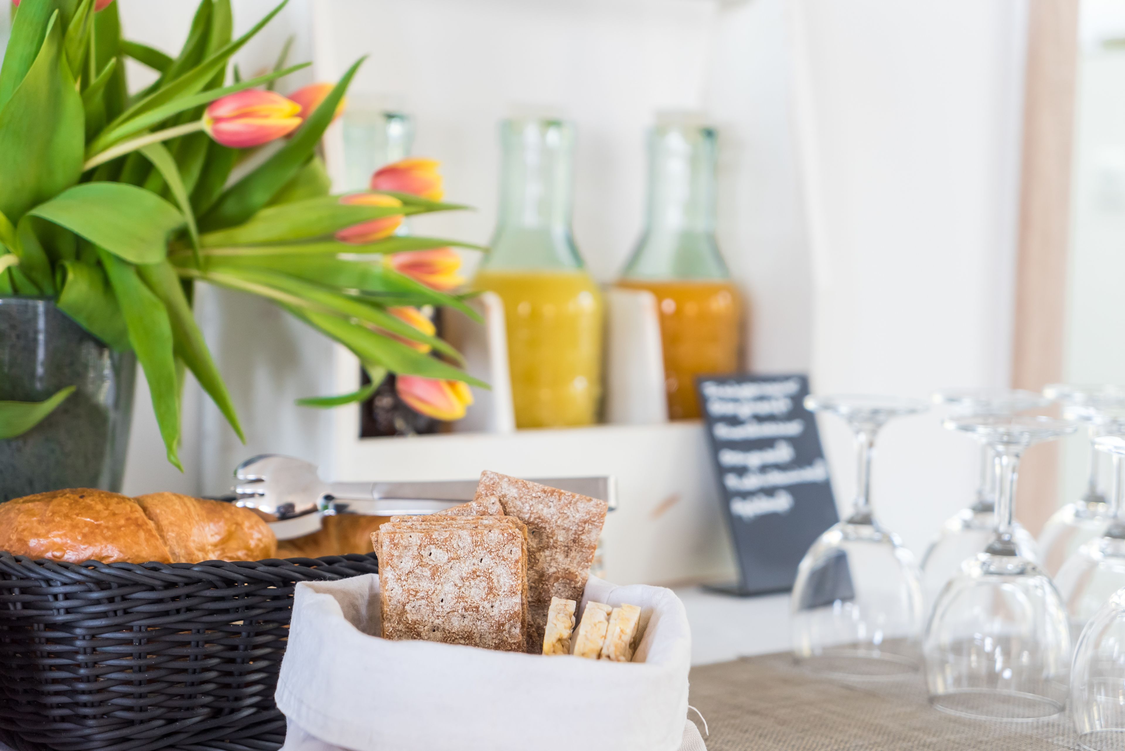 Une table avec un panier de pain, un vase de tulipes et deux bouteilles en verre.