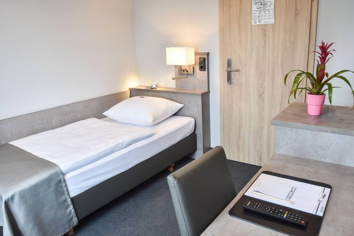 Een hotelkamer met een bed, nachtkastje, lamp en een potplant.