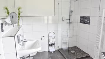 A modern bathroom with a glass shower enclosure, a white sink, and a towel rack.